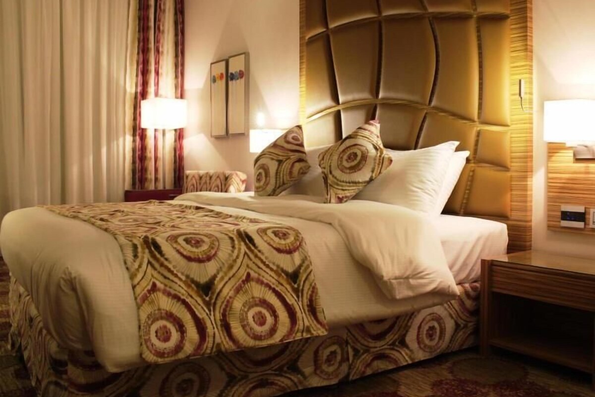 A hotel room with a large bed, a headboard with a geometric pattern, a bedside table, and a nightstand.