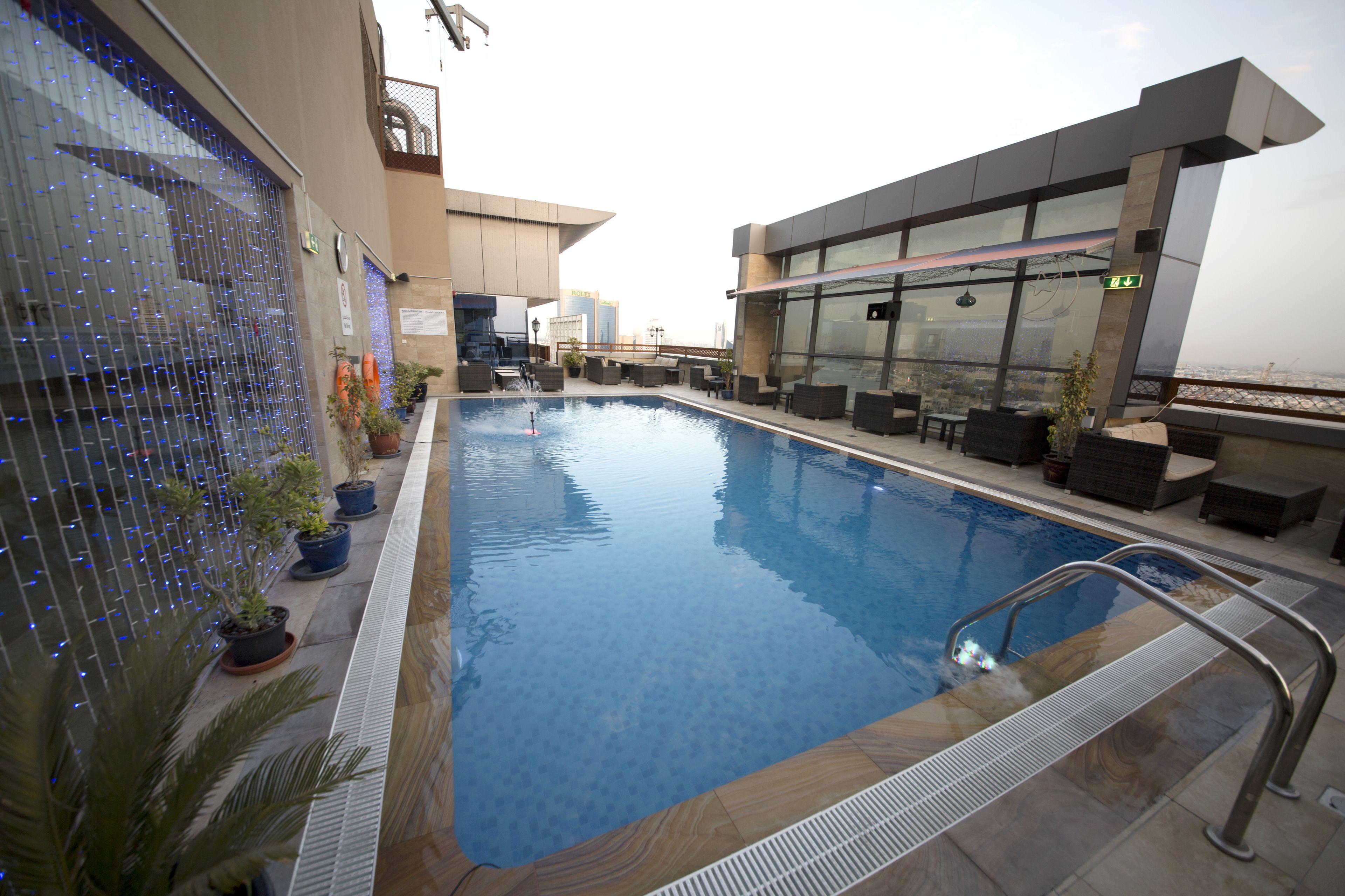 An indoor swimming pool with a view of the cityscape, surrounded by lounge areas and potted plants.