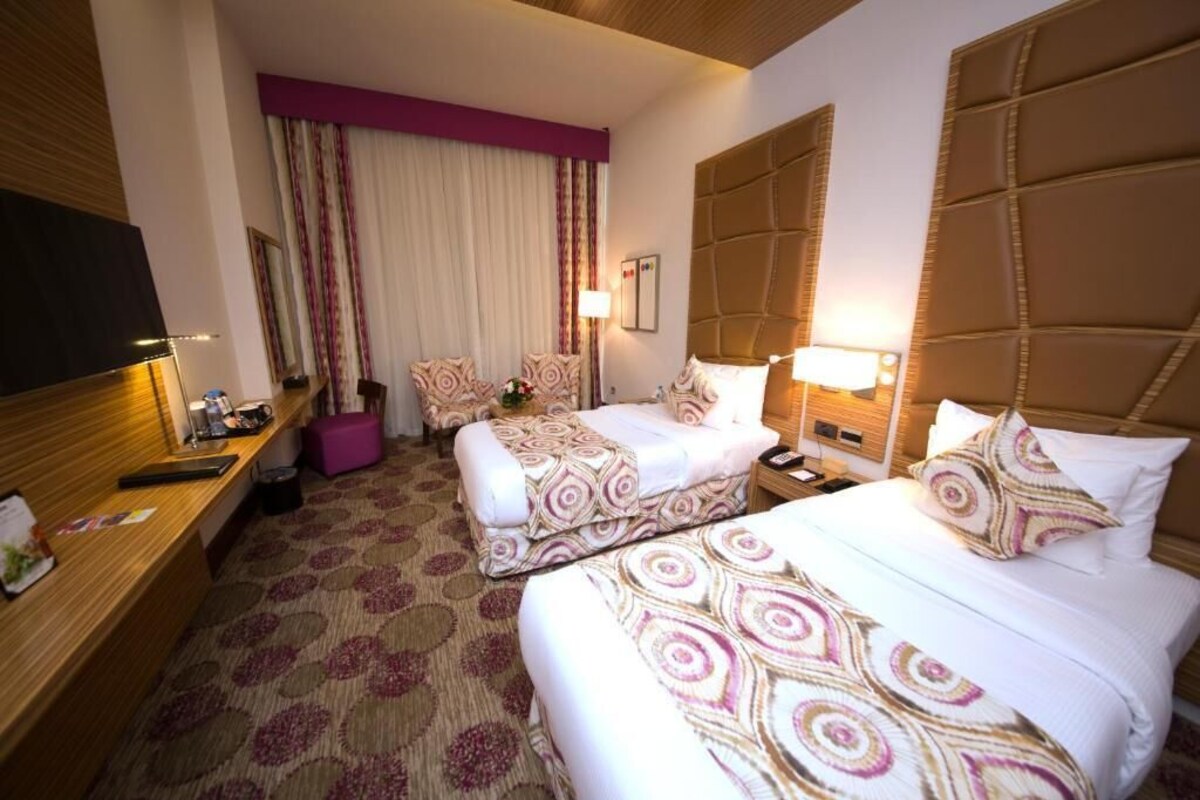 A hotel room with two beds, a desk, a TV, and a window with curtains.