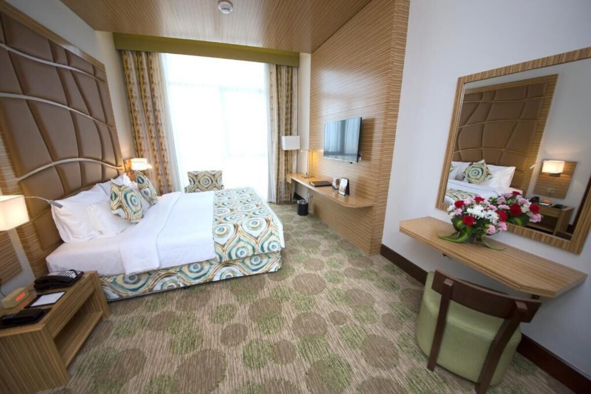 A hotel room with a large bed, a desk with a mirror, a TV, and a window with curtains.