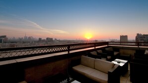 Una terraza en la azotea con el horizonte de la ciudad al atardecer, con mobiliario exterior y vistas a los edificios.