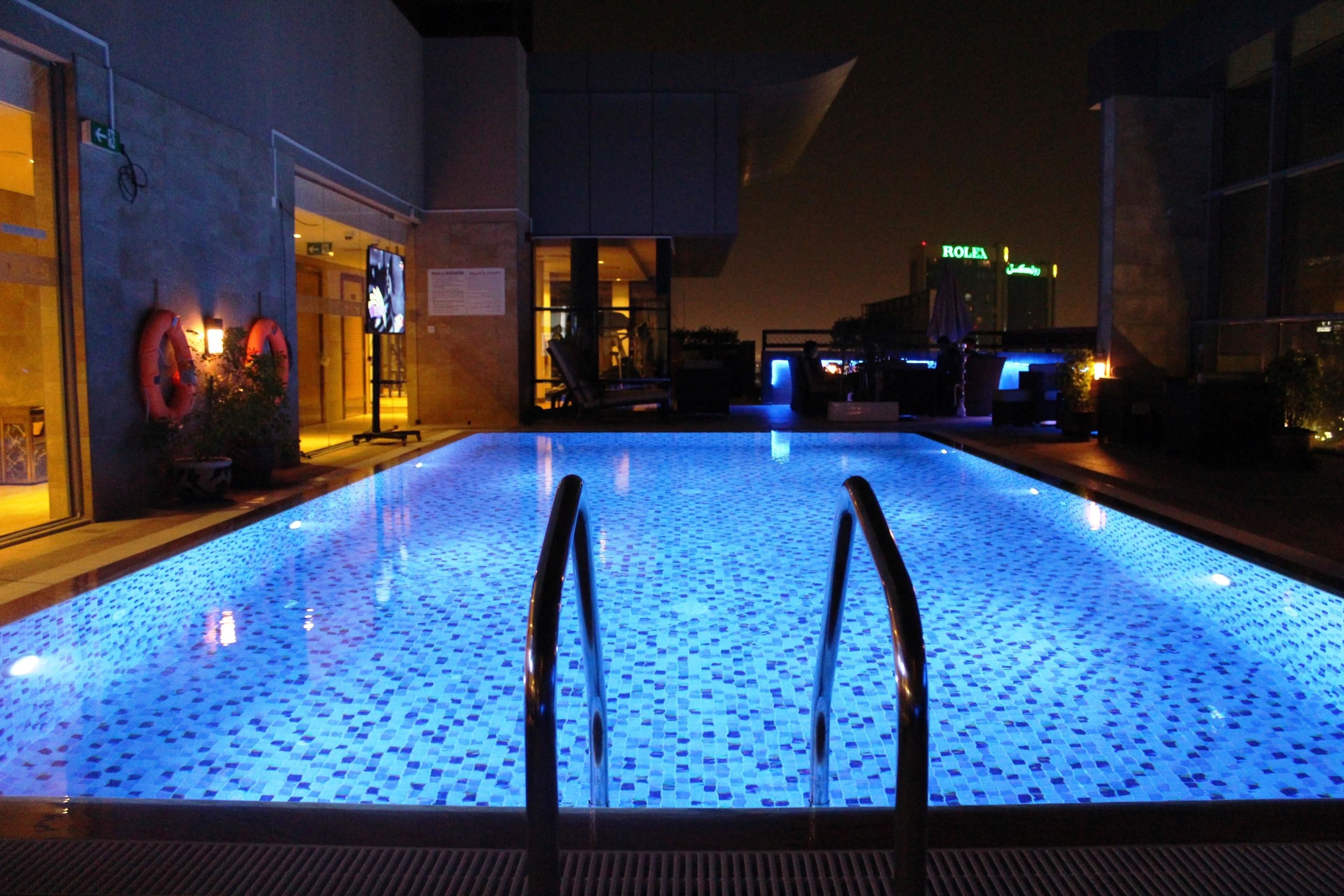 Una piscina interna con pavimento in mosaico blu e scalette metalliche.