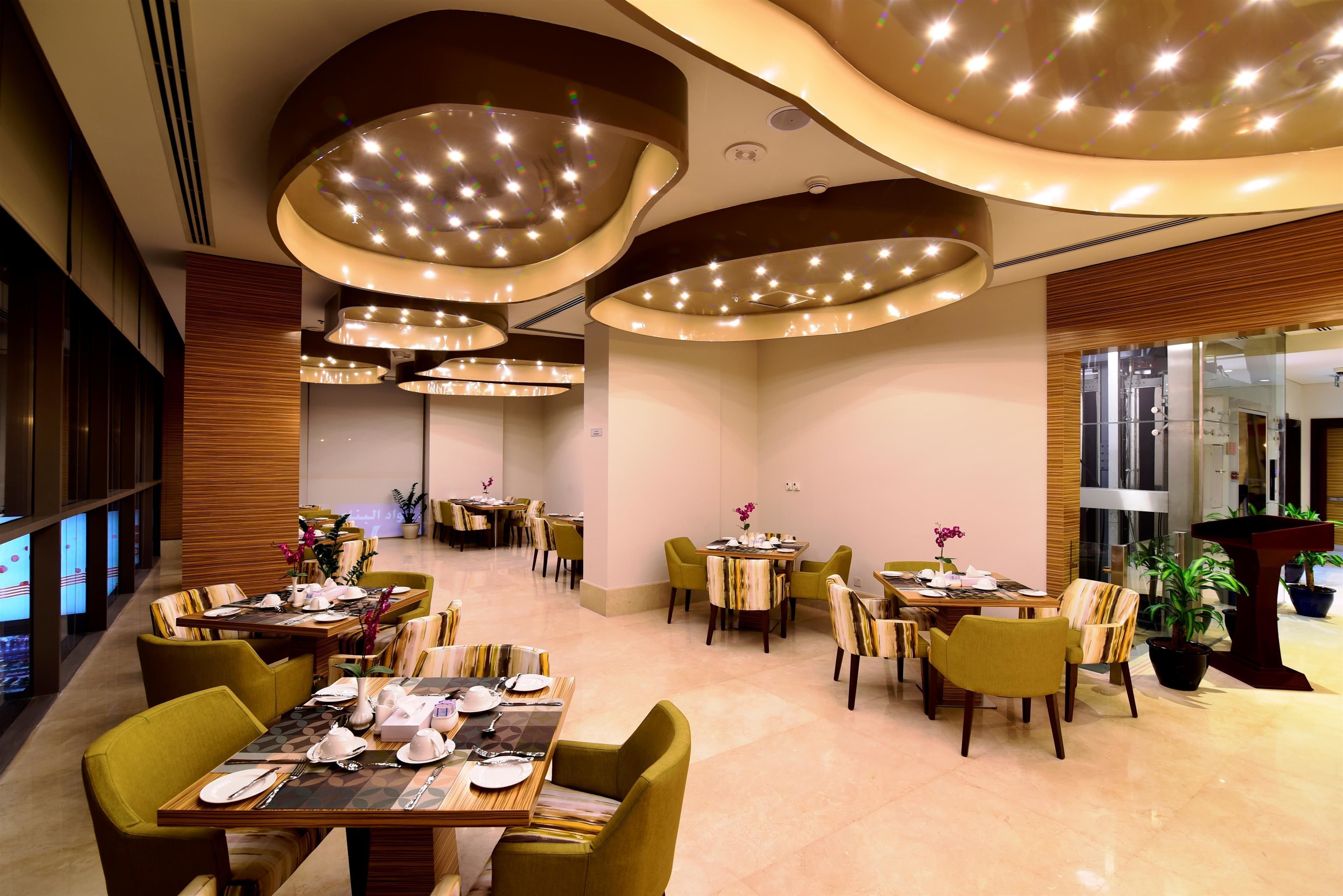 A modern restaurant with multiple dining tables and chairs, featuring a contemporary ceiling design with integrated lighting.