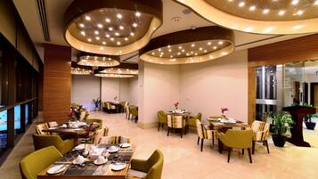 A modern restaurant with multiple dining tables and chairs, featuring a contemporary ceiling design with integrated lighting.