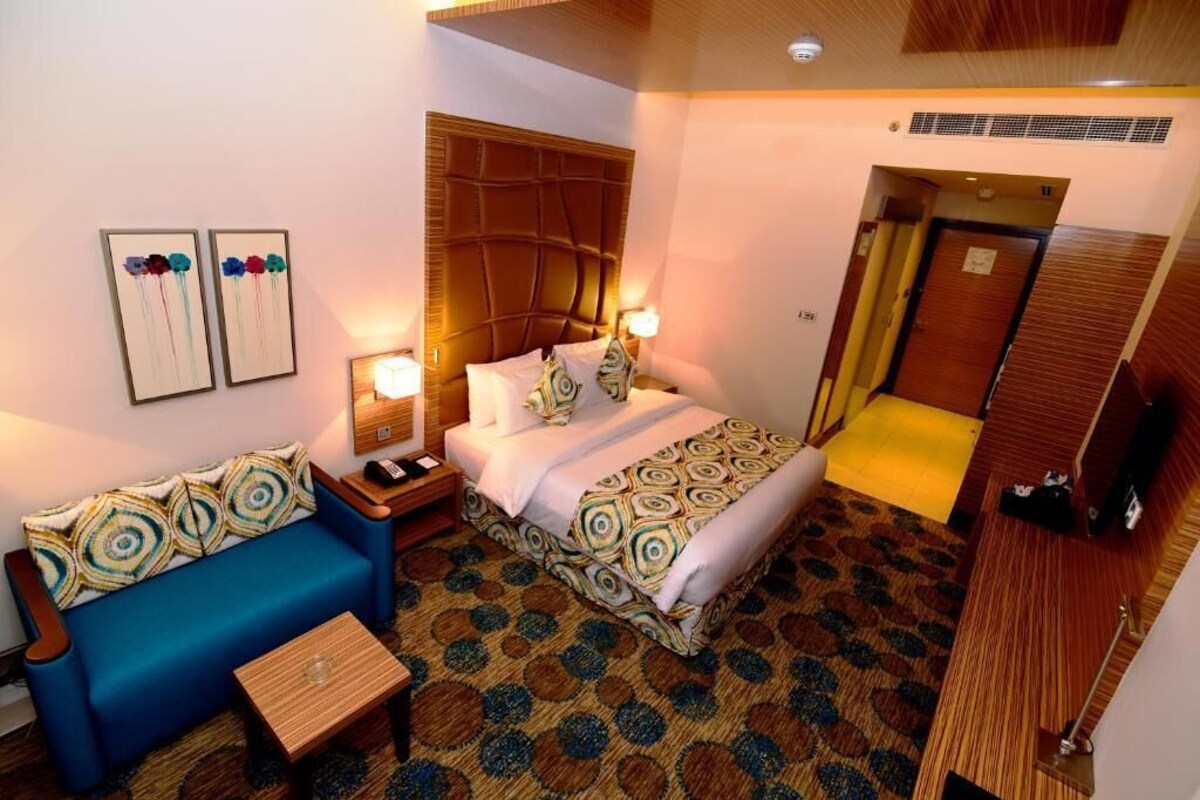 A hotel room with a bed, a blue sofa, a small table, and a patterned carpet.