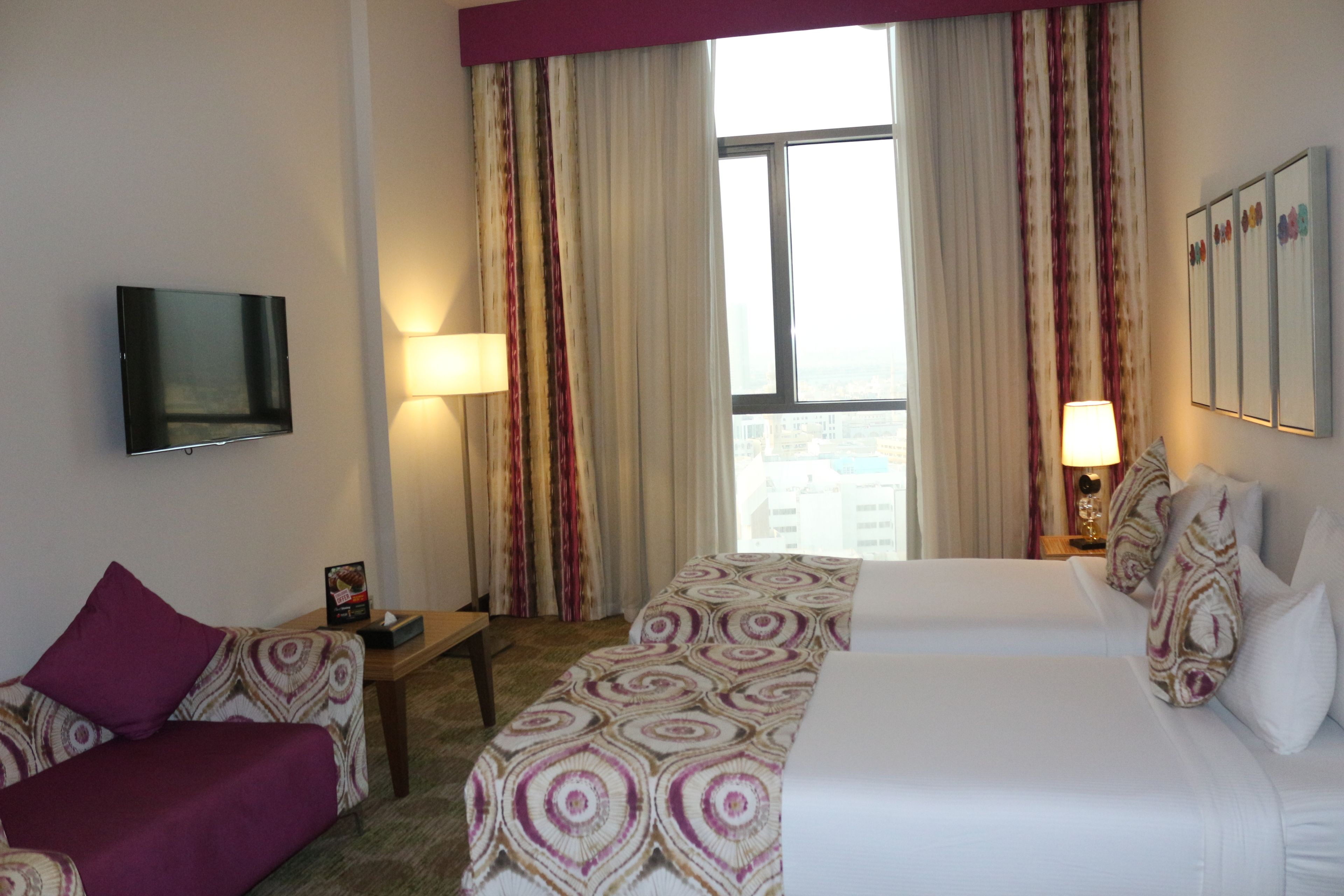 Une chambre d’hôtel avec deux lits, une télévision, un bureau et une fenêtre avec des rideaux.