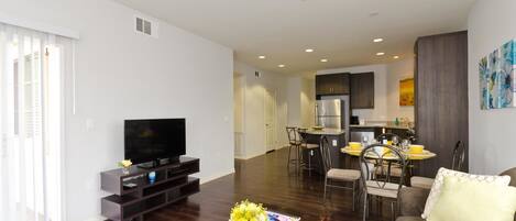 A modern living room with a flat-screen TV, a coffee table with a vase, a sofa, and a dining area with chairs and a table.