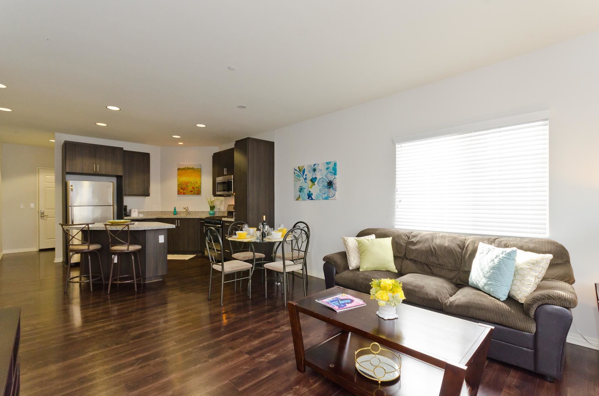 A modern living room with a brown sofa, a coffee table, and a dining area with chairs and a small island.