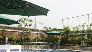 Uma área de piscina com espreguiçadeiras e guarda-sóis, cercada por vegetação e um muro decorativo.