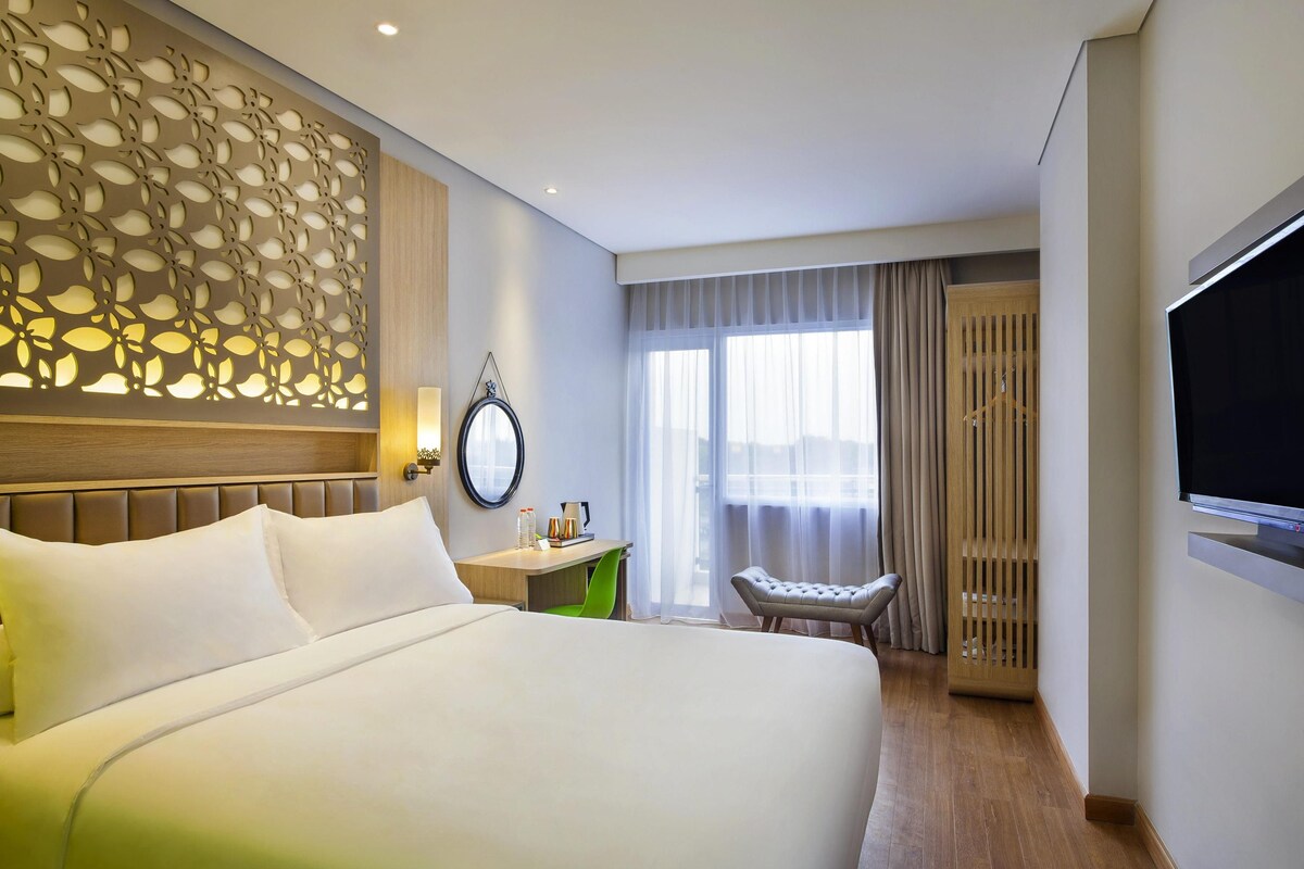 A hotel room with a large bed, a desk, a chair, a TV, and a window with curtains.
