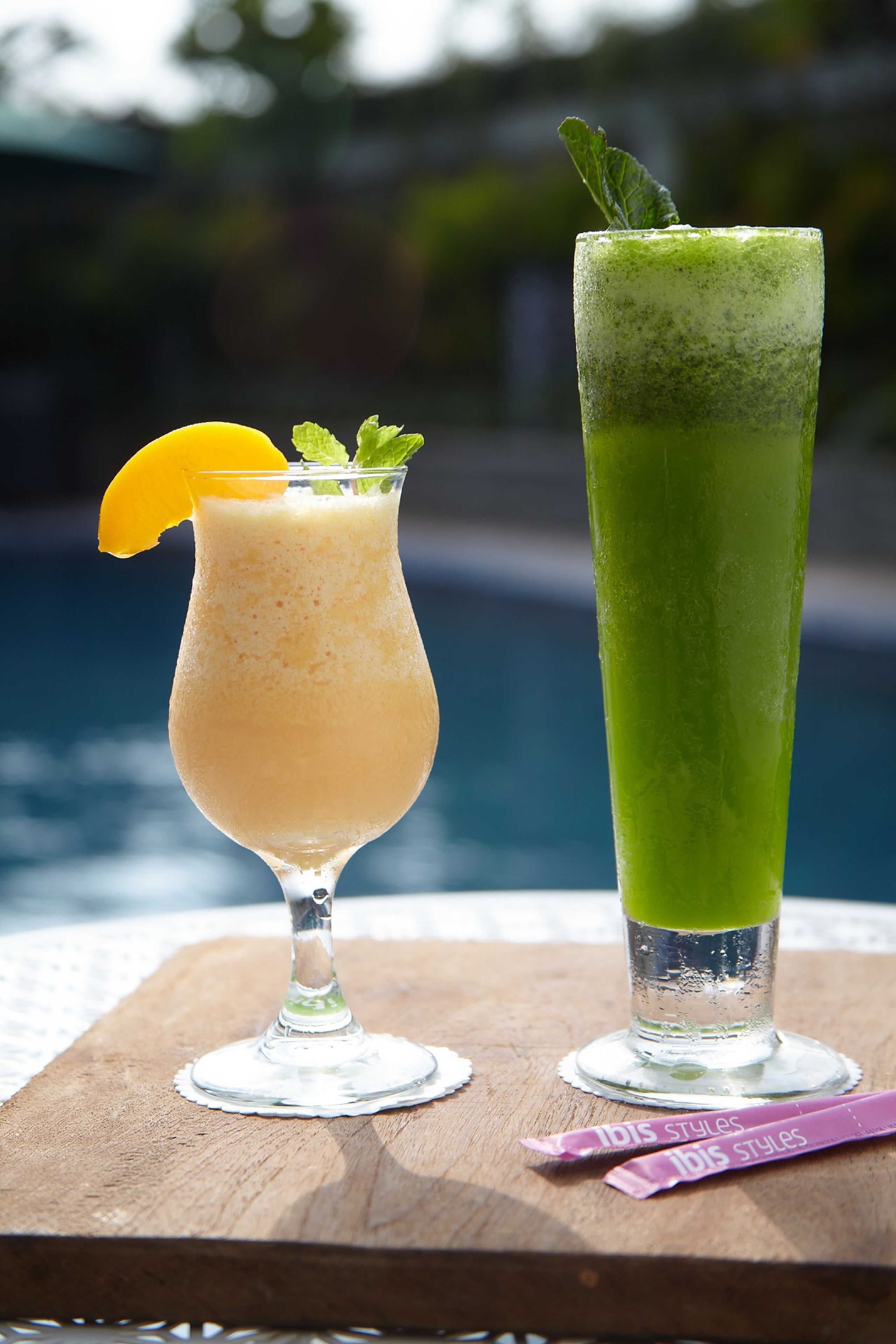 Dos bebidas sobre una mesa de madera junto a una piscina.