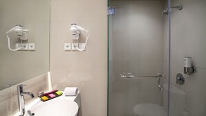 A modern bathroom with a glass-enclosed shower, a white sink with a mirror, and a towel rack. - Ibis Styles Cikarang (Cikarang)