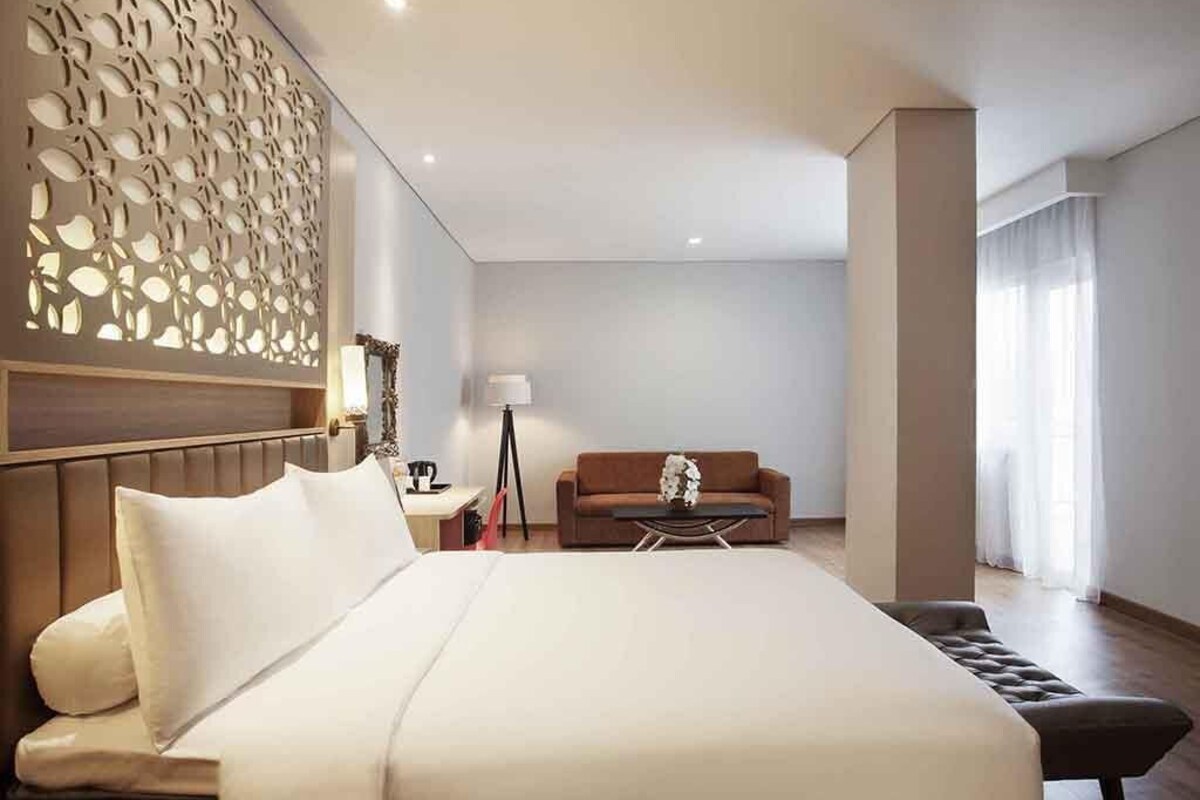 A hotel room with a large bed, a sofa, a small table, and a decorative wall panel.