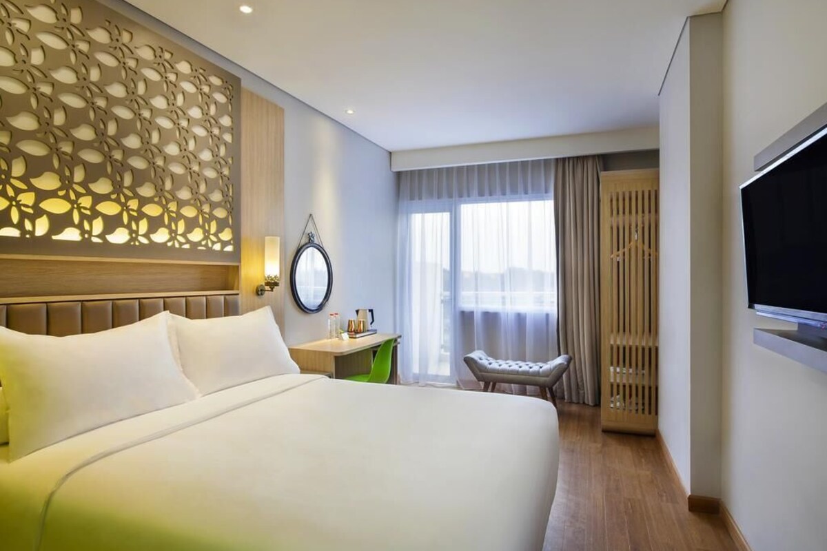A hotel room with a large bed, a desk, a chair, a TV, and a decorative wall panel.