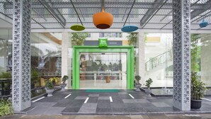 Uma entrada moderna com porta verde, plantas em vasos e um pilar com padrão decorativo.