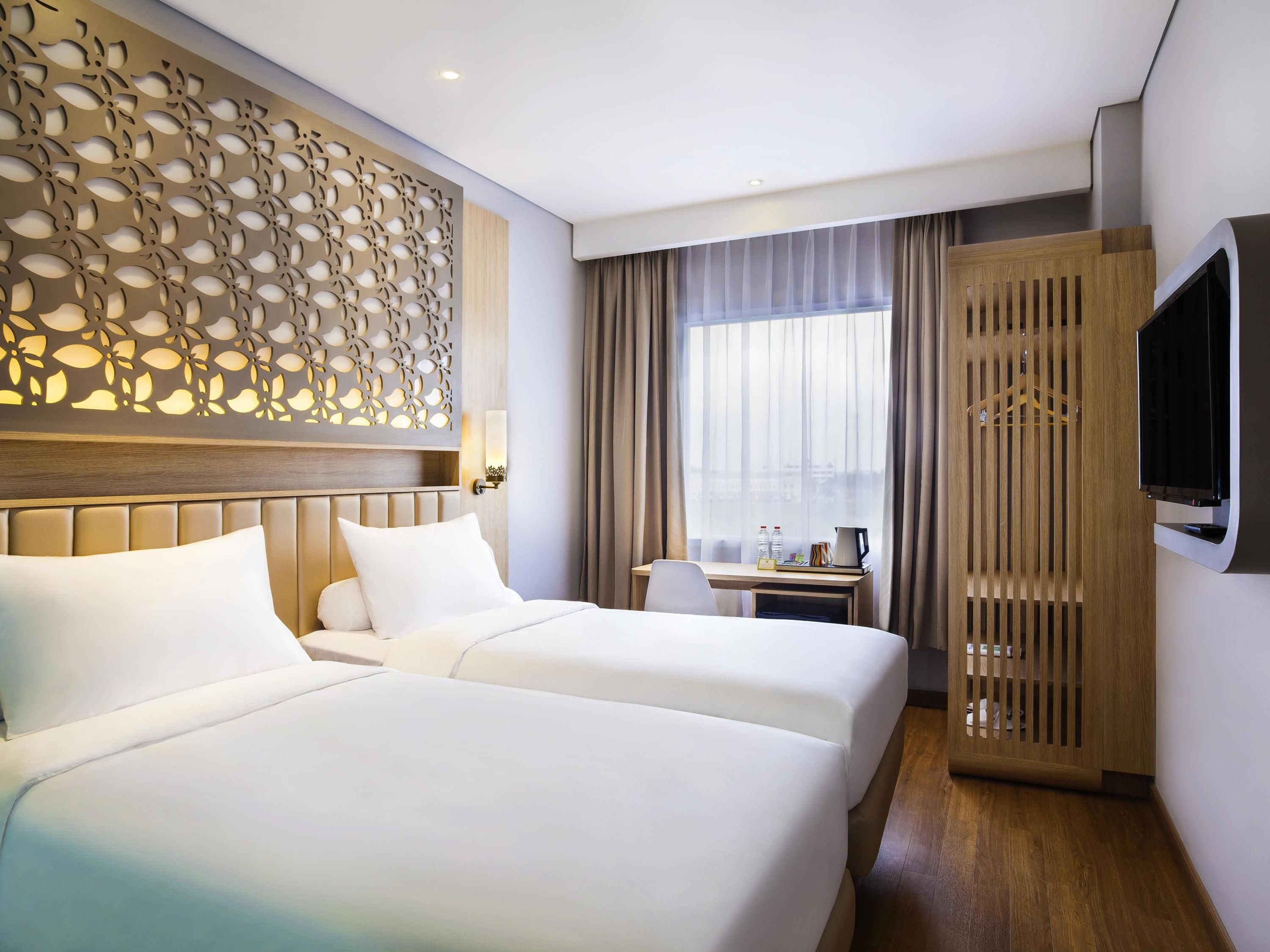 A hotel room with two beds, a desk, a TV, and a decorative wall panel.