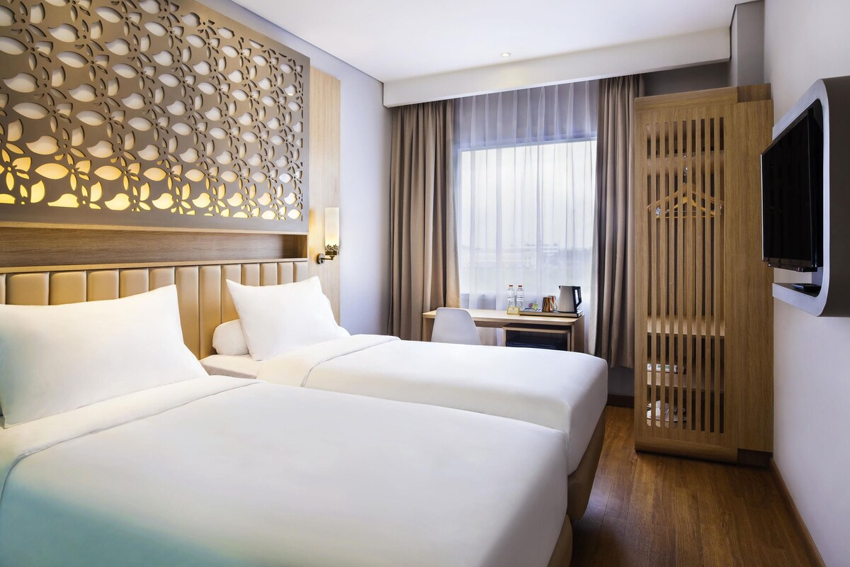 A hotel room with two beds, a desk, a TV, and a decorative wall panel.