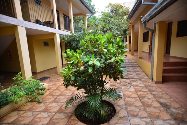 A courtyard with a central potted plant, tiled flooring, and a building with balconies and stairs.