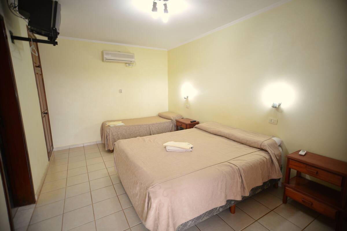 Une chambre d’hôtel avec deux lits, une télévision, la climatisation et une table de chevet avec une lampe.