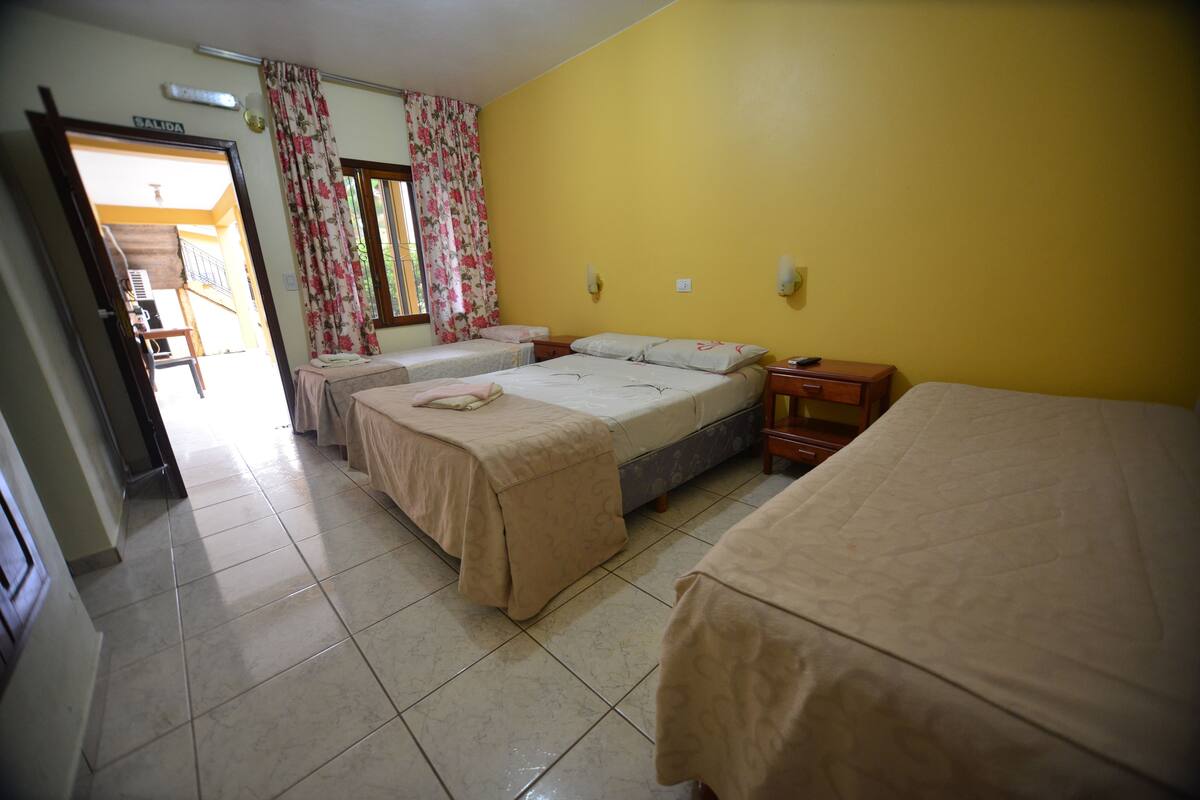 Une chambre d’hôtel avec trois lits, une table de chevet en bois et une porte donnant sur un balcon.