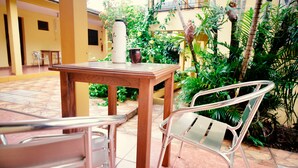 Une table en bois avec un thermos et une tasse, deux chaises en métal et une rambarde en verre.