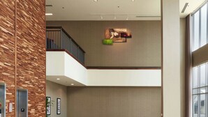 A spacious lobby with a high ceiling, a wooden accent wall, a seating area with a sofa and chairs, and a staircase leading to an upper level. - Courtyard by Marriott Rome (Rome)