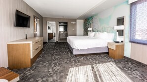 A modern hotel room with a large bed, a flat-screen TV mounted on the wall, a desk with drawers, a vanity with a mirror, and a bathroom visible through an open door. - Courtyard by Marriott Rome (Rome)