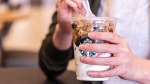 A person holding a Starbucks drink with a spoon.