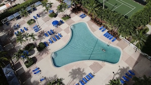 An aerial view of a resort with a large swimming pool, sun loungers, a tennis court, and palm trees. - Sunny Isles Suites (Sunny Isles Beach)