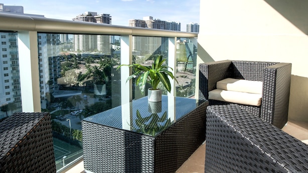A balcony with a glass table, wicker furniture, and a potted plant. - Sunny Isles Suites (Sunny Isles Beach)