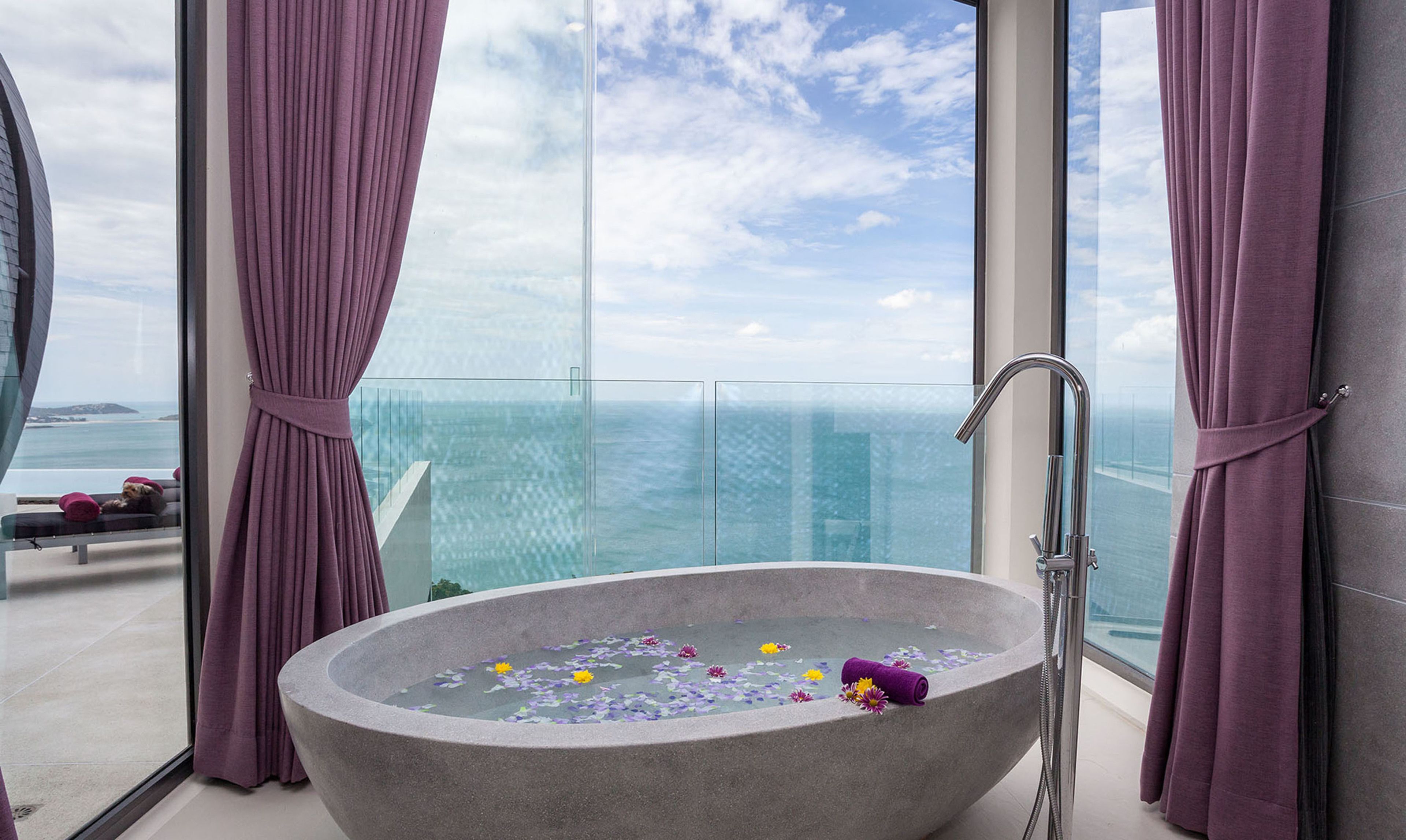 Un baño moderno con una bañera independiente, ducha con mampara de vidrio y vista al océano.
