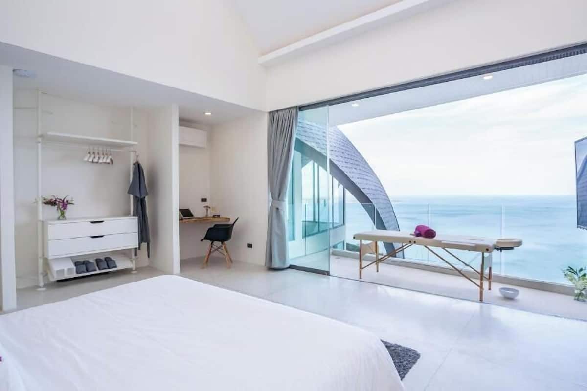 Une chambre moderne avec un grand lit, un bureau et un balcon offrant une vue sur la mer.