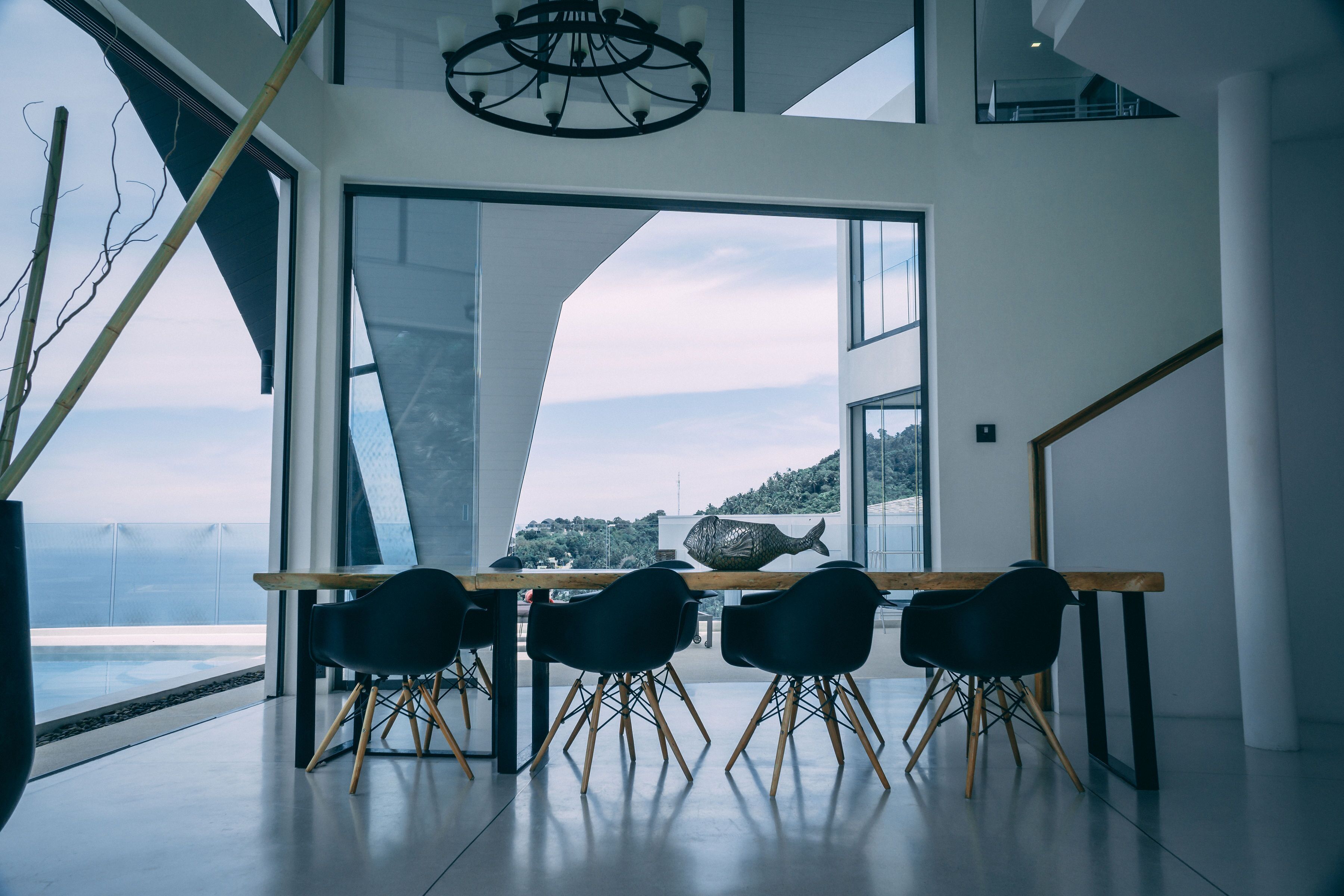 Un espace de salle à manger moderne, doté d’une grande table et de quatre chaises, d’un lustre et offrant une vue sur la mer.
