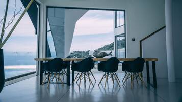 Un espace de salle à manger moderne, doté d’une grande table et de quatre chaises, d’un lustre et offrant une vue sur la mer.