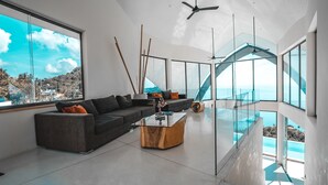 A modern living room with a large sectional sofa, a glass coffee table, and a view of the ocean through large windows. - Sky Dream Villa (Koh Samui)