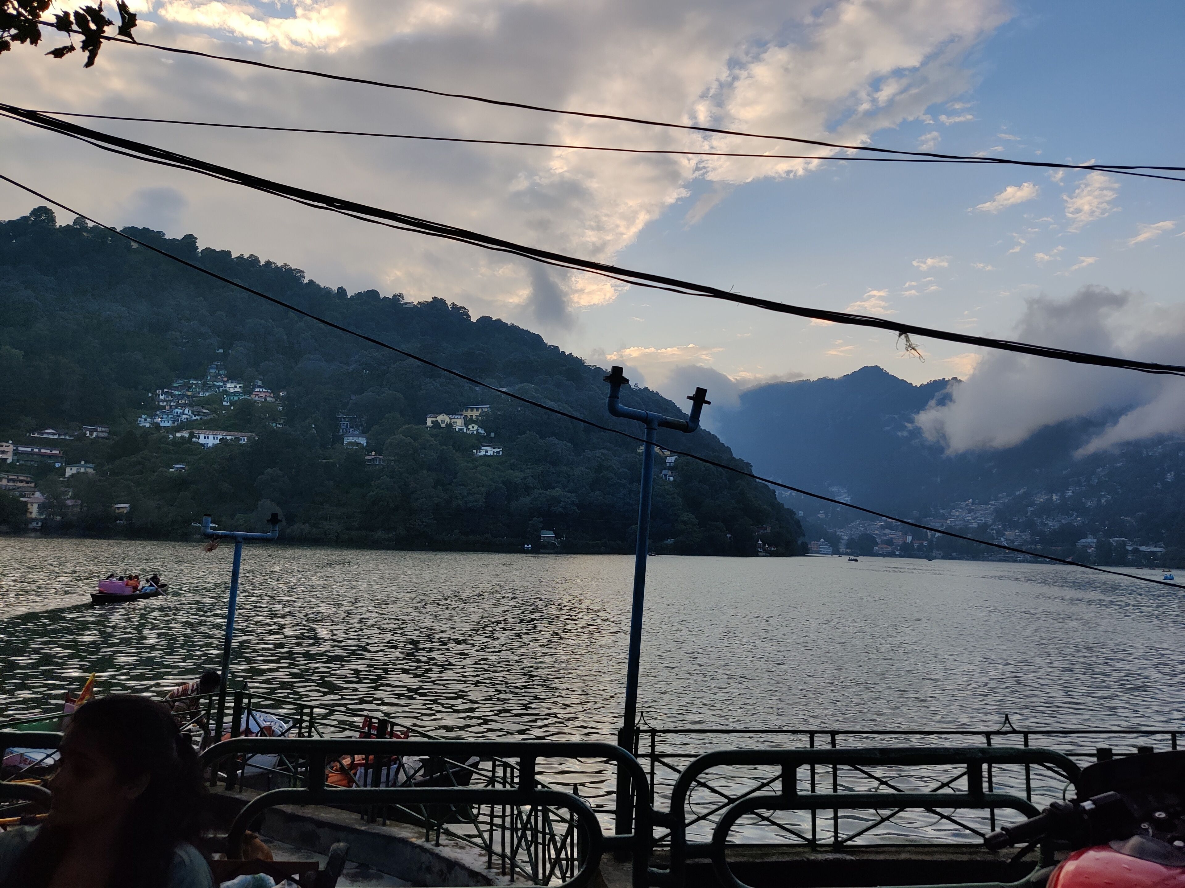 A lake with a boat docked on the shore, surrounded by hills and houses.