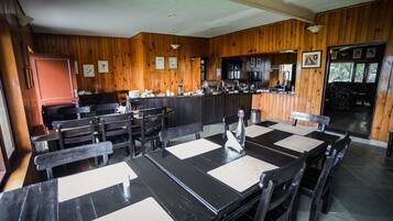 Un restaurante con paredes de madera, una zona de bar y mesas con sillas negras.