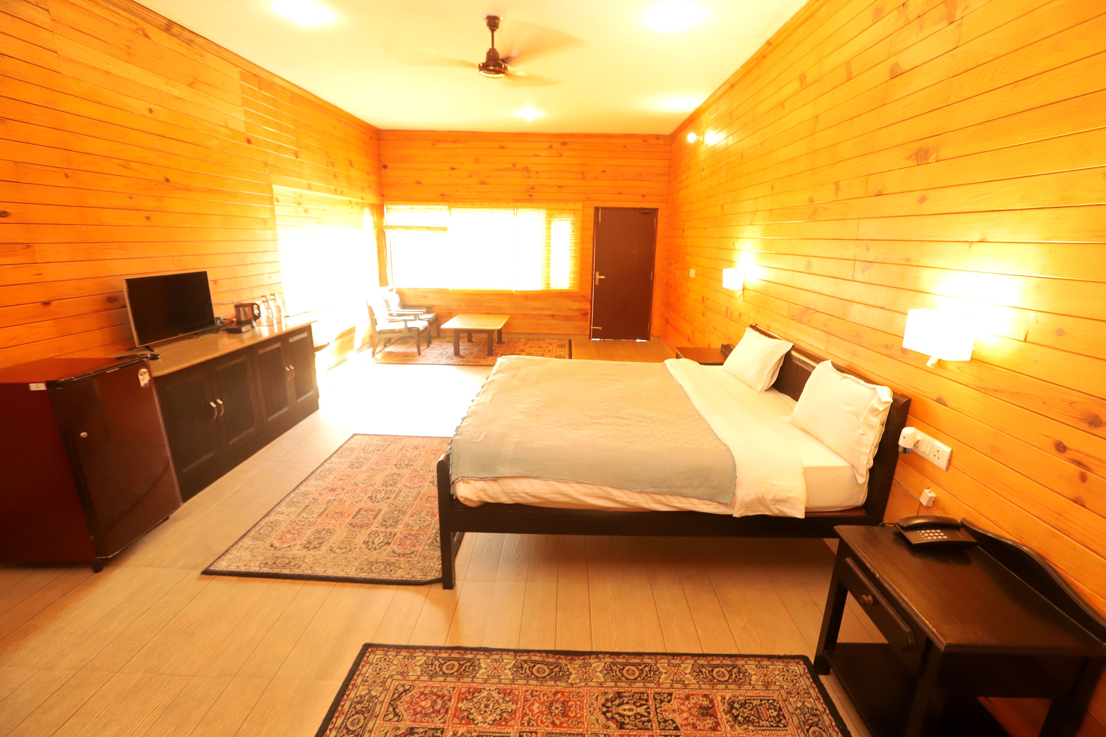 A room with wooden walls, a bed, a desk, a chair, a television, and a window.