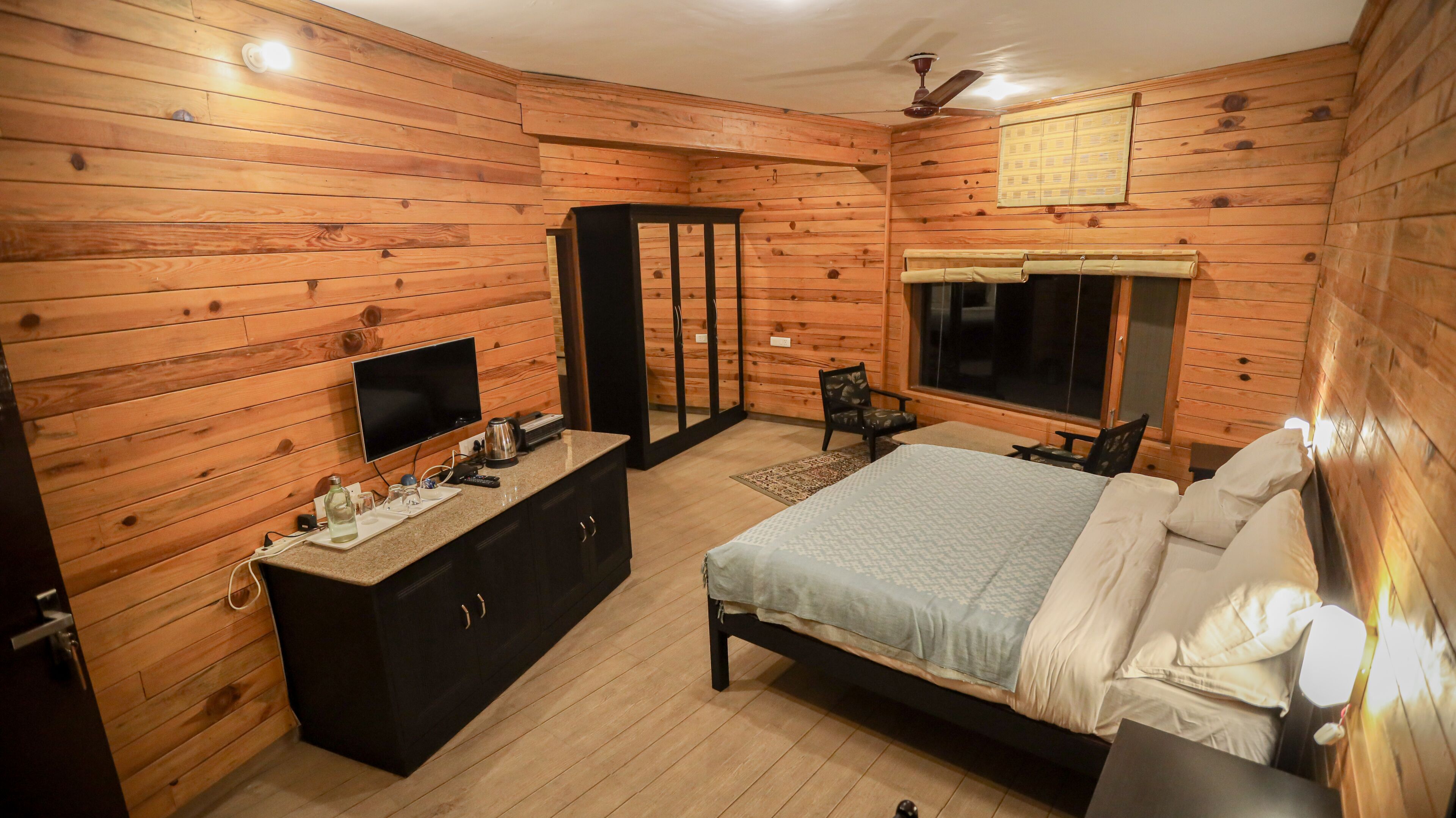 Un dormitorio con paneles de madera, una cama, un televisor, un escritorio y una ventana.