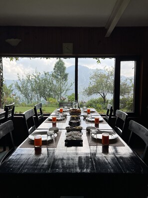Mesa de jantar posta para uma refeição, com vista para montanhas e árvores.