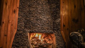 Ein Steinkamin mit Feuer, umgeben von Holzwänden und einem gemusterten Teppich.