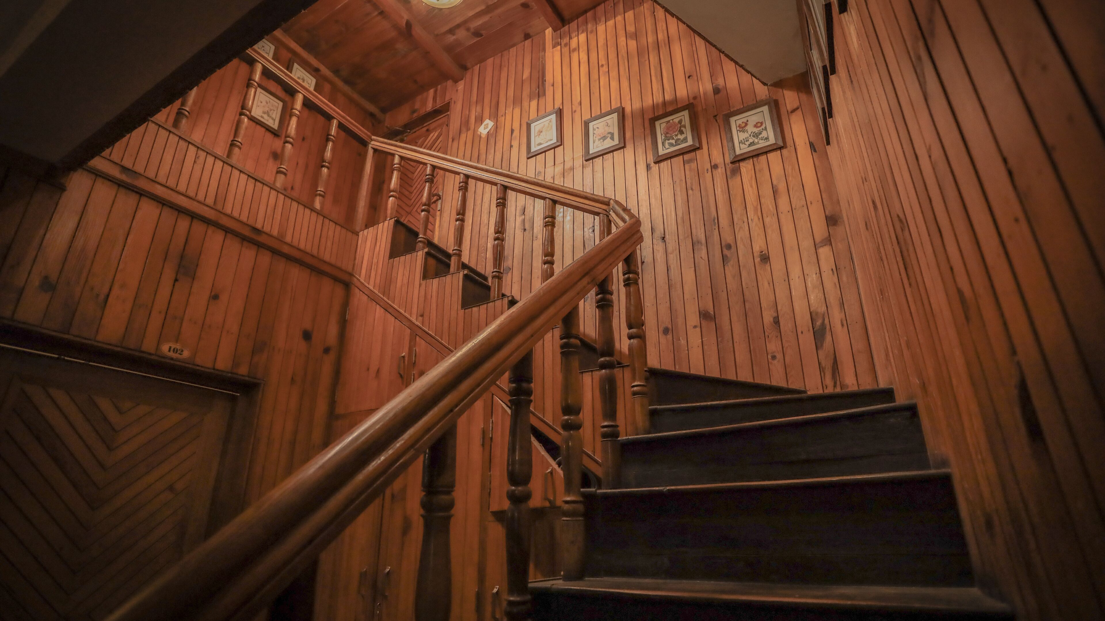 Una escalera de madera con barandilla, paredes de madera y cuadros enmarcados.
