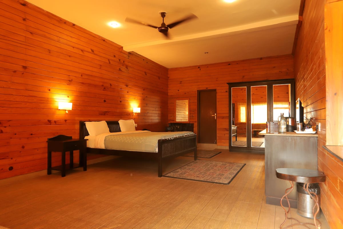 Une chambre aux murs lambrissés, comprenant un lit, des tables de chevet, un ventilateur de plafond et un petit coin cuisine.