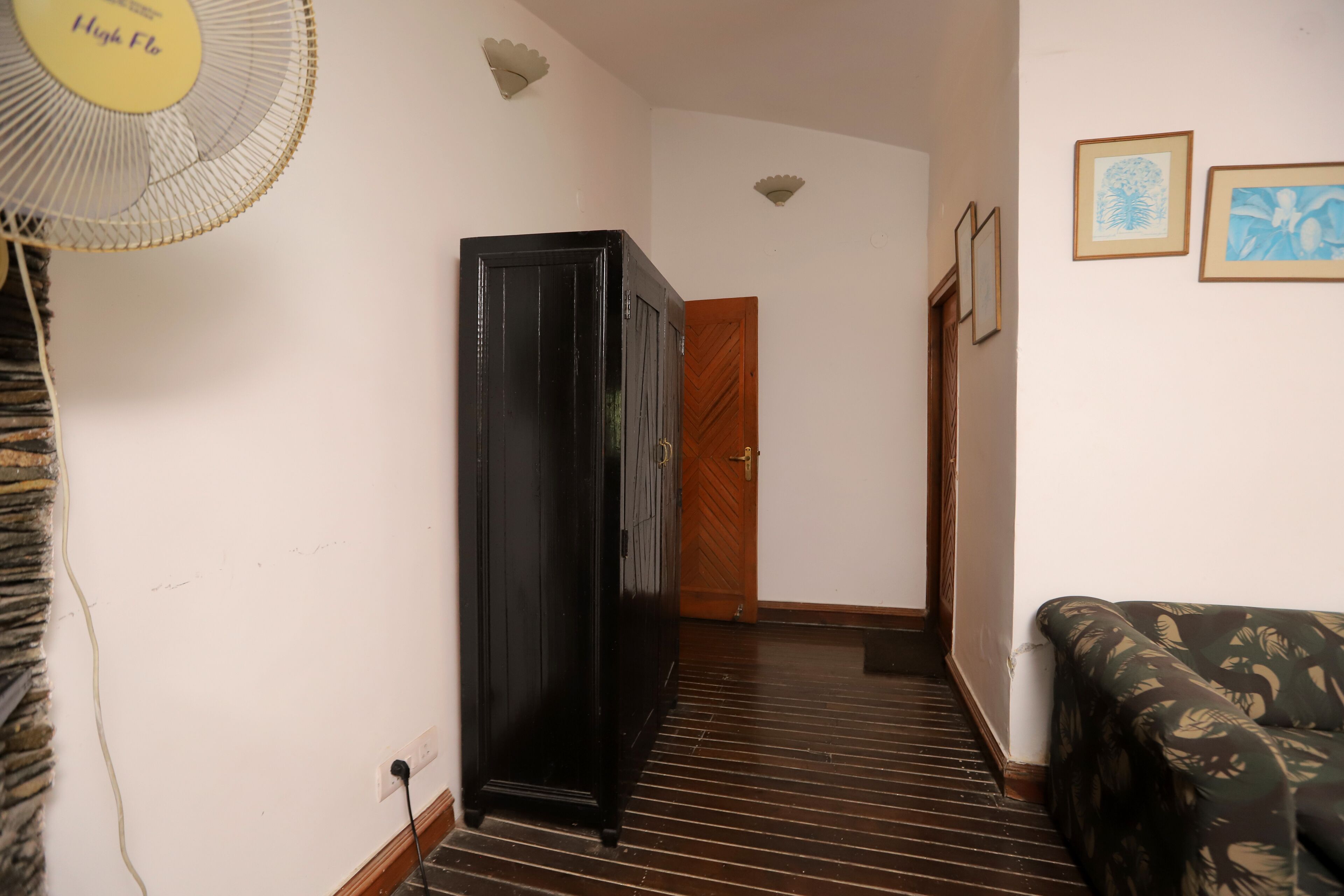 A hallway with a wooden floor, a black cabinet, a wooden door, and a patterned sofa.
