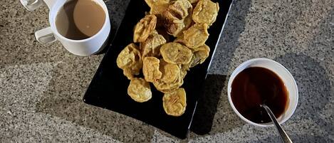A table with a black tray holding fried snacks, two white cups of coffee, a small bowl of sauce, and a blue object.