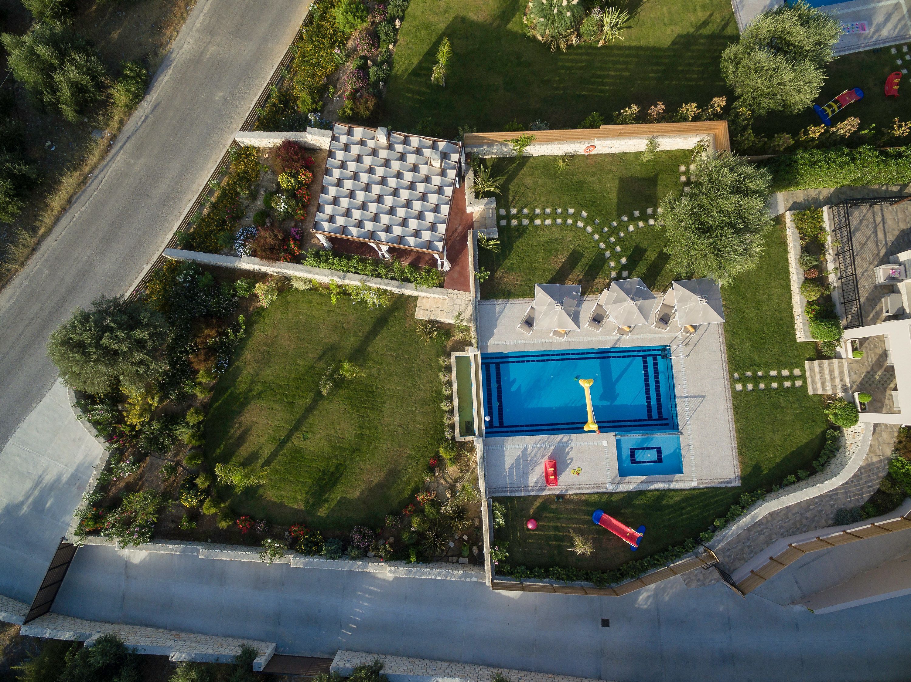 Ein Luftbild eines Wohnhauses mit Schwimmbad, einer Terrasse mit Sonnenschirmen und einem gepflegten Garten.