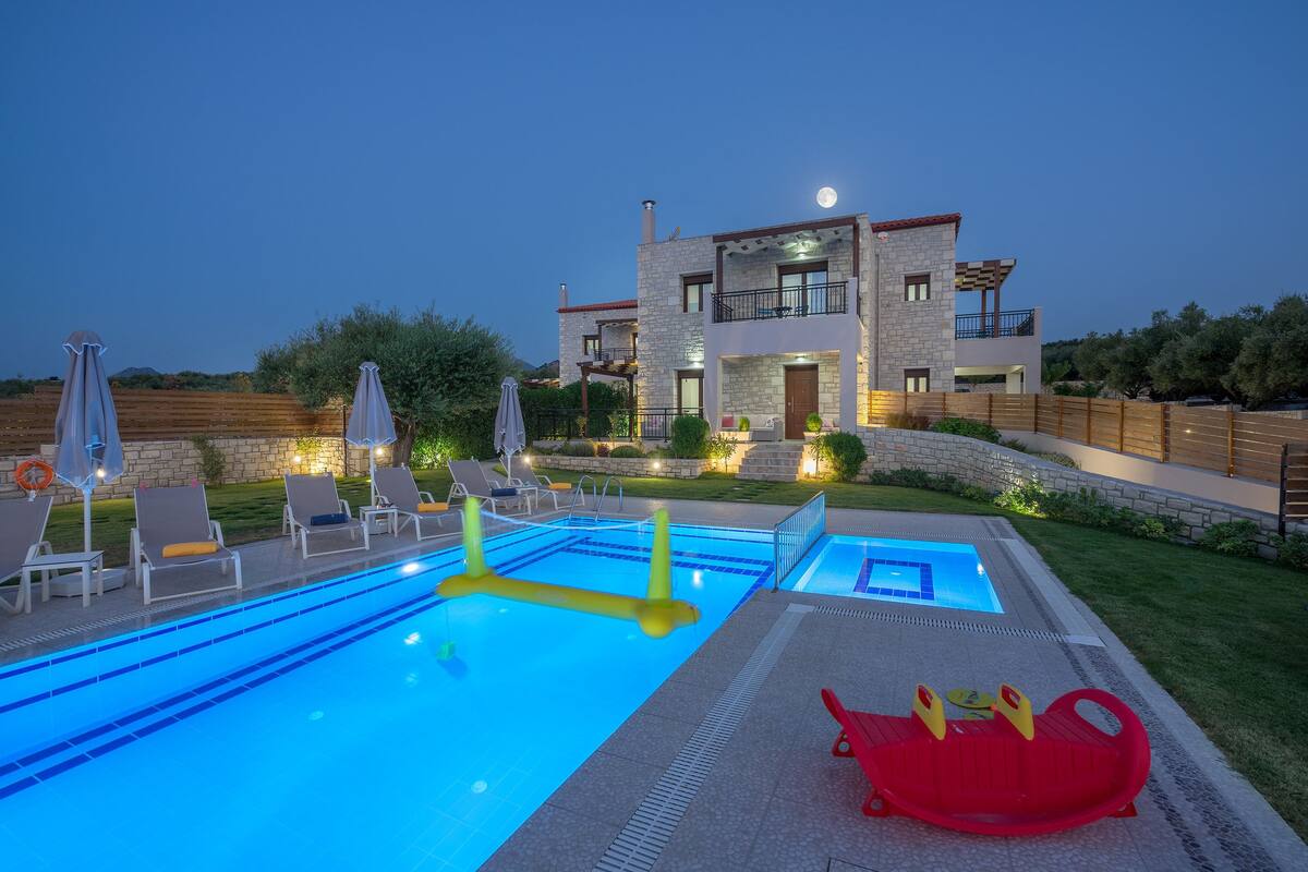 Ein modernes, zweistöckiges Haus mit Swimmingpool, Liegestühlen und einem roten Spielbereich für Kinder.