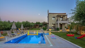 A swimming pool with lounge chairs and a house in the background. - Olive Garden Villas (Mylopotamos)