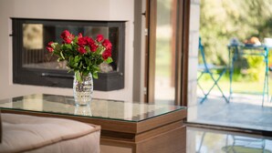 A modern living room with a glass-top coffee table, a beige sofa, and a vase of red roses. - Olive Garden Villas (Mylopotamos)