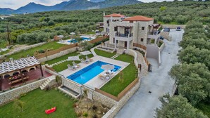A modern villa with a swimming pool, multiple balconies, and a view of the surrounding mountains. - Olive Garden Villas (Mylopotamos)